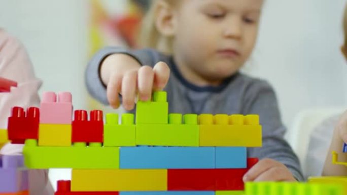 可爱的小男孩用桌上的彩色砖块建造玩具屋
