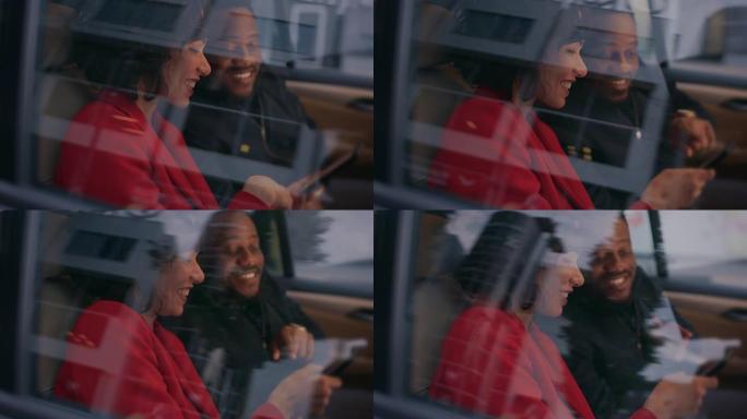 美丽的女人和她的男性伴侣坐在汽车的后座上，他们共享智能手机屏幕，聊天，玩得开心。今天是大城市的夜晚。
