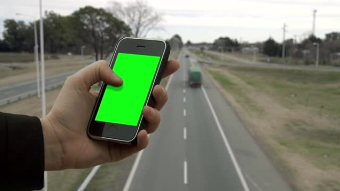 男性双手在高速公路上的桥上握着智能手机绿屏。