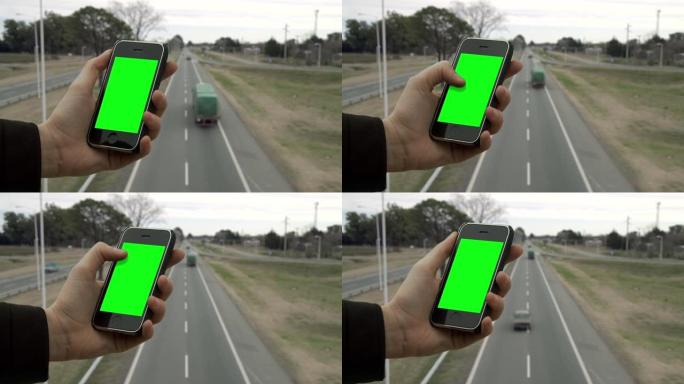 男性双手在高速公路上的桥上握着智能手机绿屏。