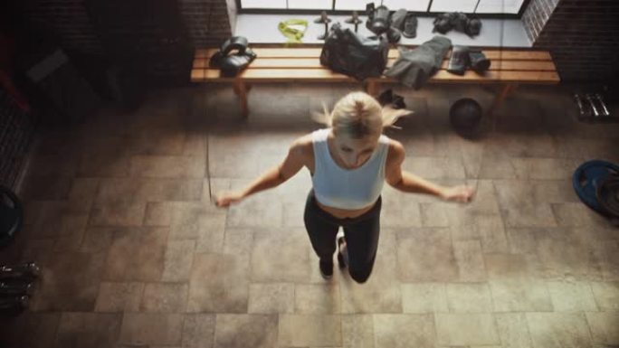 在硬核健身房穿着运动服和跳绳的运动美女。使用跳绳有氧运动进行健身训练。顶视图相机拍摄