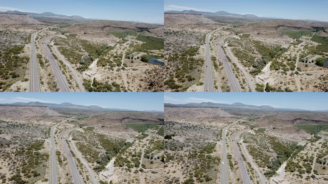 美国亚利桑那州夏季雄伟的沙漠岩石、丘陵、道路和晴朗天空的史诗空中全景。公路旅行概念。
