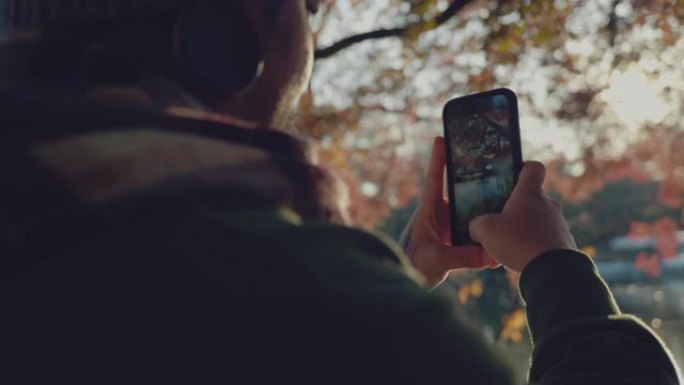 亚洲旅游男子在手机上拍摄湖泊和枫树的照片。