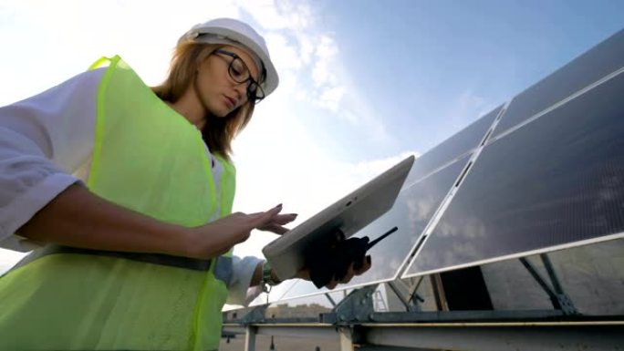 戴眼镜的女太阳能工程师正在用她的计算机站在太阳能电池板旁边工作