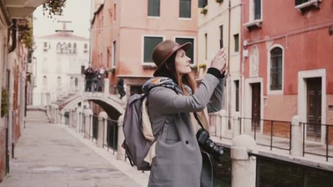 快乐美丽的旅游女孩在意大利威尼斯惊人的水渠街慢动作拍摄智能手机照片。