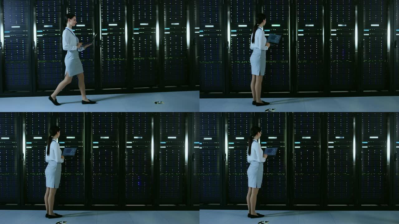美丽的数据中心女it技术人员带着笔记本电脑走过服务器机架走廊。她停下来，目视检查工作中的服务器机柜。