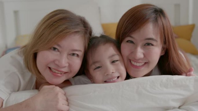 三代女性的肖像看着相机摆姿势拍摄全家福，可爱的小女孩拥抱妈妈和奶奶享受在家中的时光，微笑的母亲，女儿