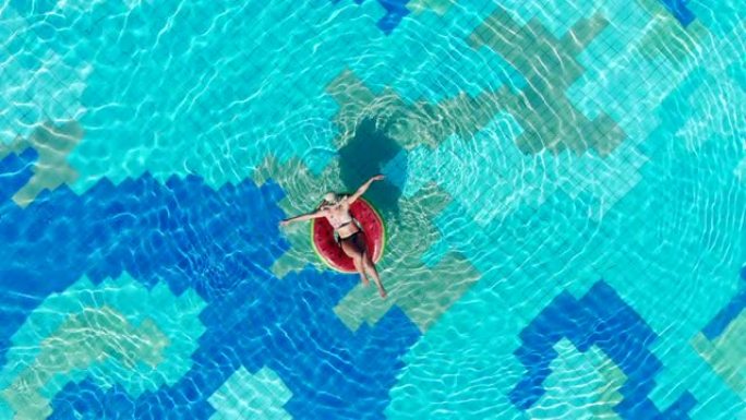 橡胶圈上的年轻女子在蓝色的游泳池里放松。