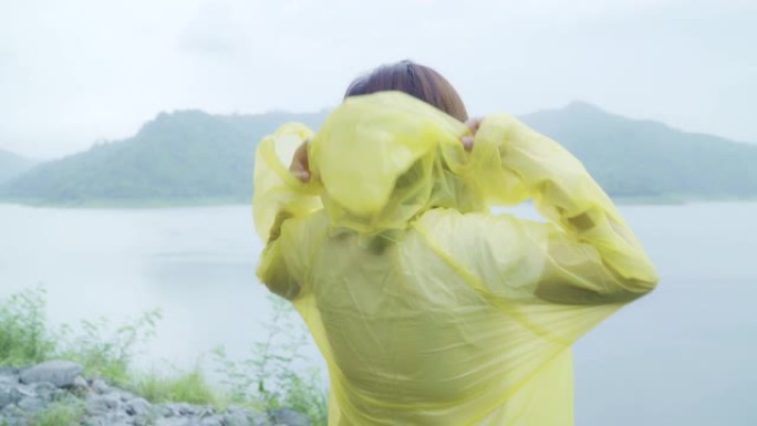 年轻的亚洲女子穿着雨衣站在湖边，在雨中玩耍时感到快乐。生活方式女性在雨天享受和放松。