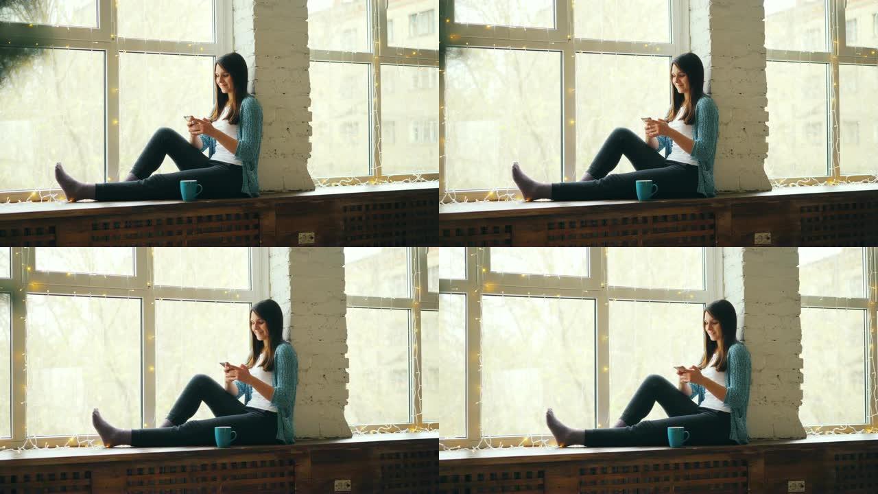 开朗的年轻女子正在使用坐在窗台上的智能手机，在家里放松并享受现代技术。人和小玩意概念。