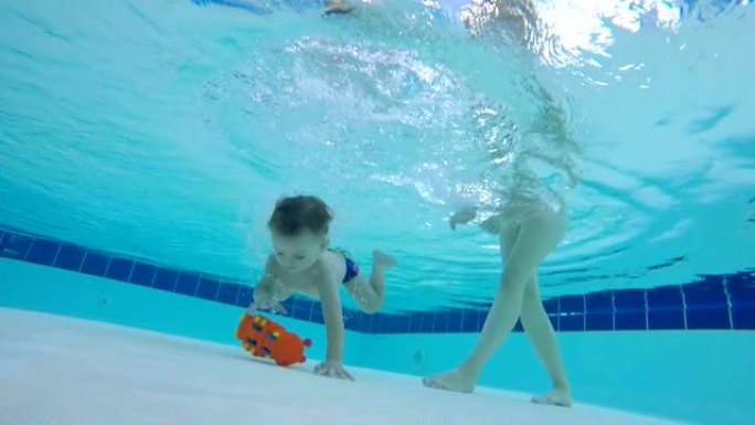 孩子的母亲帮助他从游泳池底部拿玩具