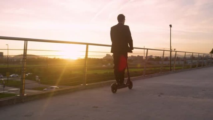 镜头耀斑: 年轻的商人喜欢在美丽的日落时骑踏板车回家。