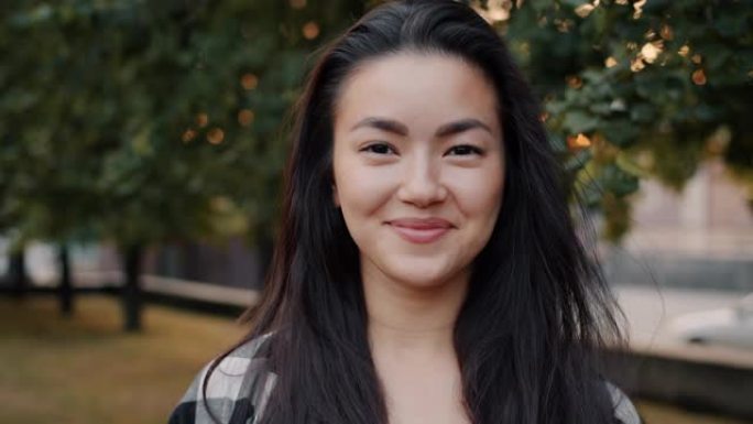 美丽的亚洲学生独自站在城市公园微笑的特写肖像