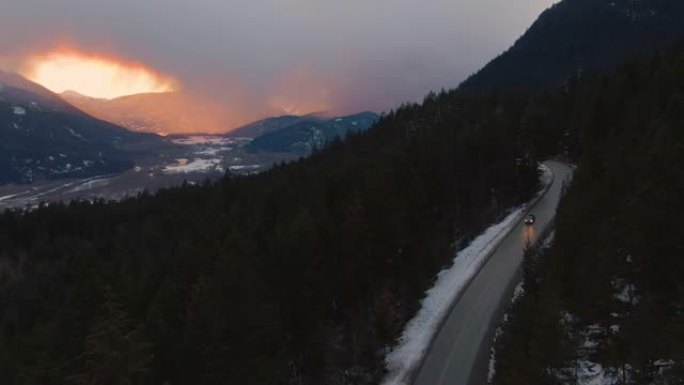 无人机: 橙色的日落照亮了森林，汽车沿着风景秀丽的高速公路行驶