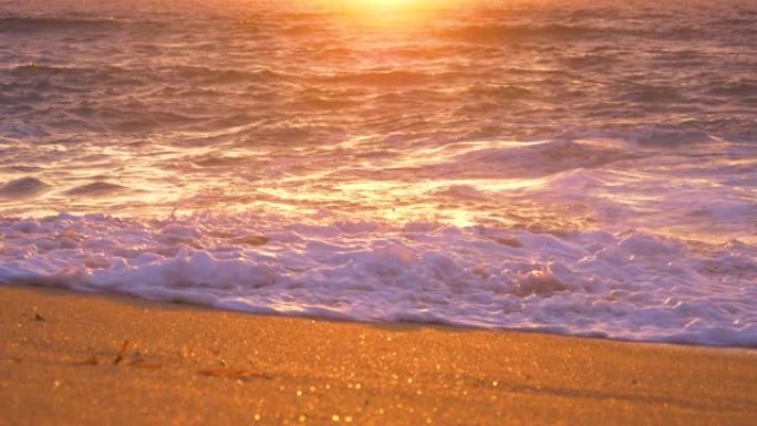 慢动作: 金色的阳光照耀着平静的海洋，冲刷在沙滩上。