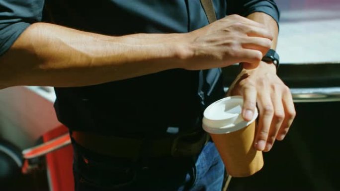 男子在4k街上用咖啡杯检查智能手表