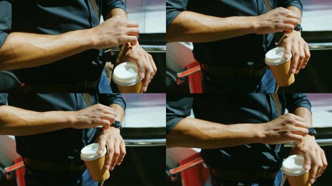 男子在4k街上用咖啡杯检查智能手表