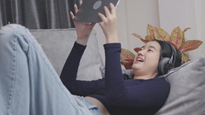 亚洲少女使用数字平板电脑进行视频通话，并与她的朋友在家里冠状病毒锁定微笑，远离距离。她在vlog社交