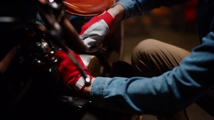 年轻英俊的机械师正在修理一辆定制的鲍勃摩托车。特写工作手套。有才华的人使用棘轮扳手。创意正宗车间车库