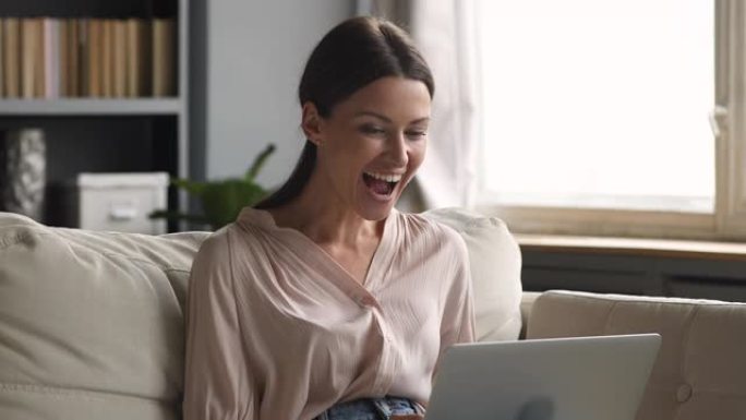 兴奋的女人坐在沙发上使用笔记本电脑获得惊人的优惠