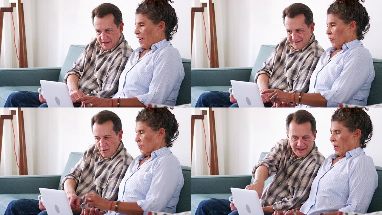 高级夫妇坐在家里的沙发上使用笔记本电脑在线购物