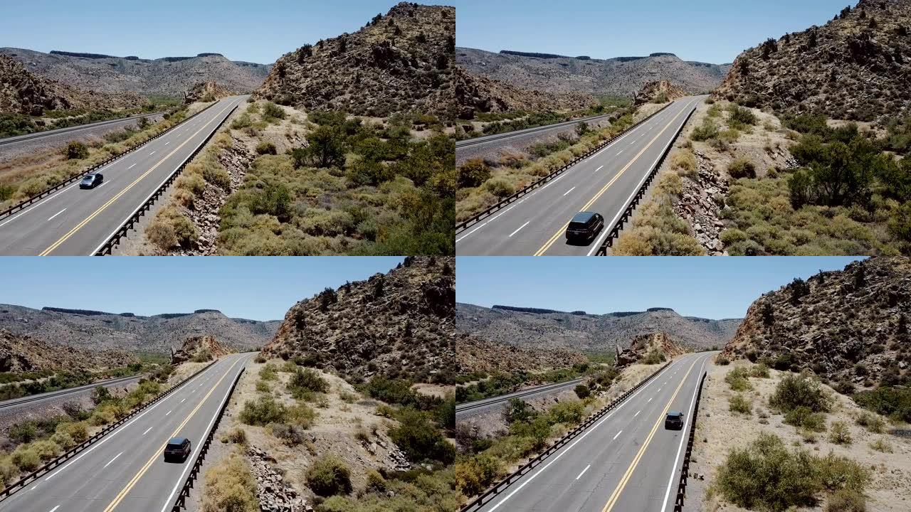 在美国亚利桑那州阳光明媚的夏天，无人机跟随银色MPV汽车沿着雄伟的阳光明媚的沙漠落基山路行驶。