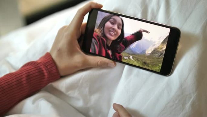 年轻女子在智能手机网络摄像头上与躺在家里床上的朋友聊天