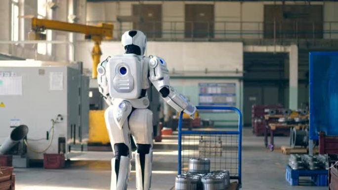 仿生机器人拉着一辆手推车，走在工厂的房间里。