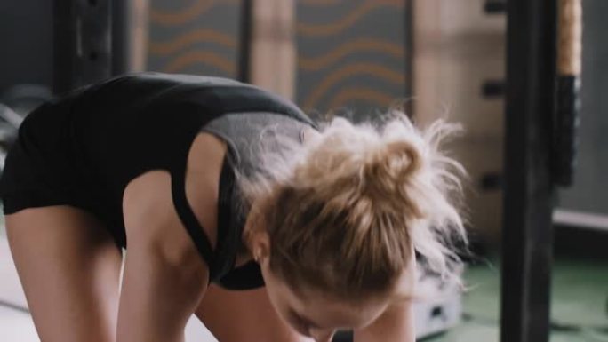 特写年轻迷人的运动金发女子用战斗绳锻炼，在大型健身房锻炼后停下来休息