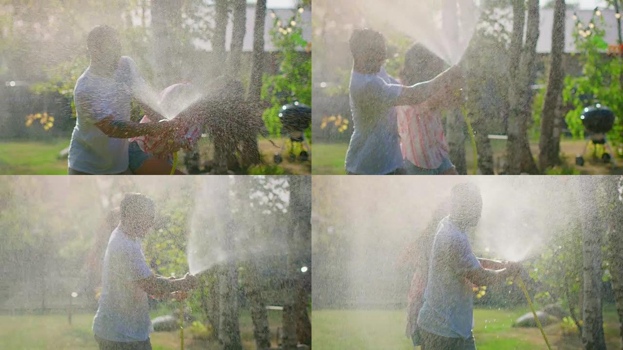 在炎热的夏日里，快乐的年轻夫妇在花园里玩水管洒水器，玩得很开心。到处喷水使它们都湿了。慢动作。