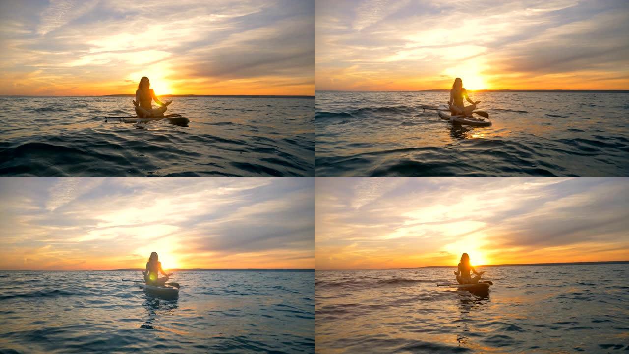 冲浪板上的冥想过程。女冲浪者漂浮在水面上时在板上冥想。