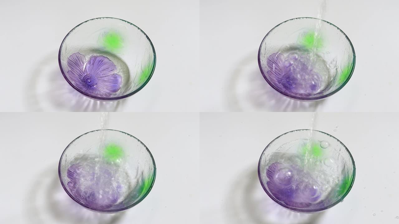 将水倒入带有紫色花朵的玻璃碗中。