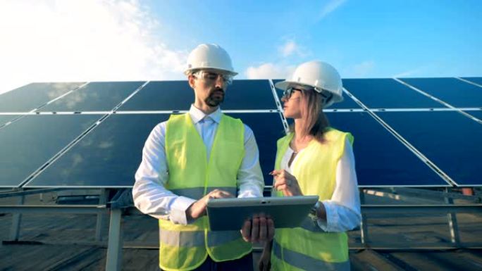 两名工人站在太阳能电池板背景上，特写镜头。
