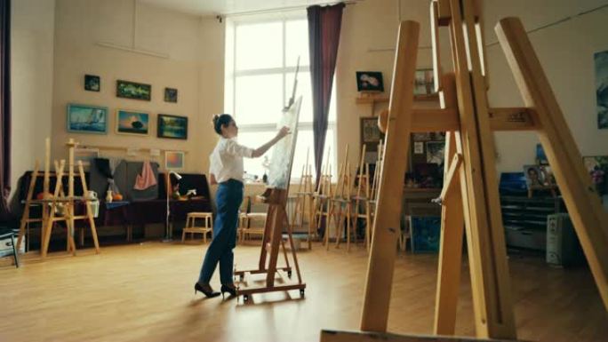 严肃的年轻女艺术家正在艺术学校教室里用画架和艺术品绘画丙烯酸颜料。创造性工作和人的概念。