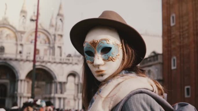 在威尼斯市广场慢动作，戴着帽子和狂欢节面具的匿名长发女人回头看相机。
