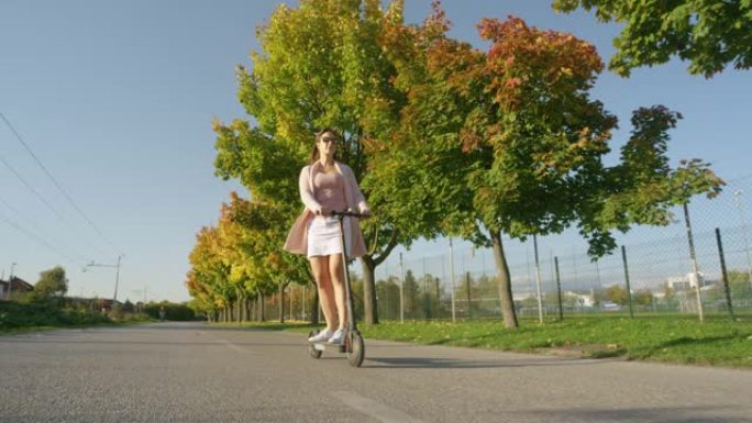 低角度: 城市女孩乘坐电动踏板车沿着风景秀丽的大道巡游。