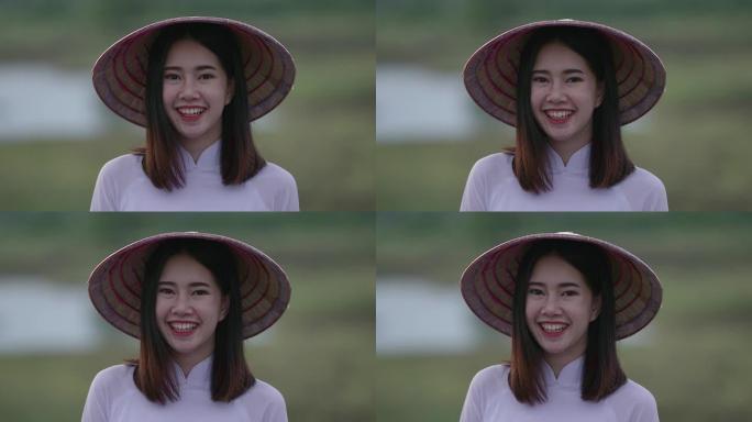 一位东南亚少年的美丽年轻女子穿着白色连衣裙，手持竹编帽子。心情愉快地站着对着镜头大笑
