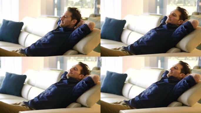 一个男人在家里的沙发上放松，抱着枕头，用帆布看电影，微笑着。