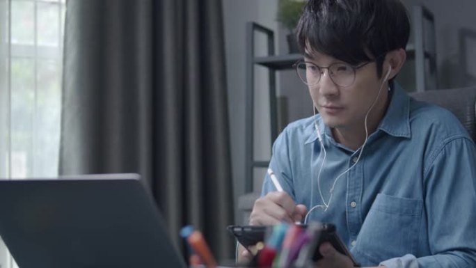有吸引力的亚洲男子使用笔记本电脑和平板电脑与他的团队在他的家庭办公室的视频会议。商人与他的合伙人谈论