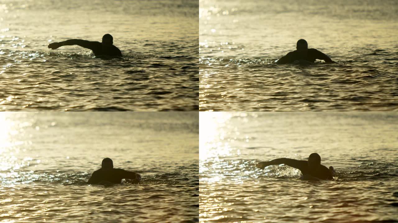 日落4k时，男性冲浪者在海上冲浪板上游泳的前视图
