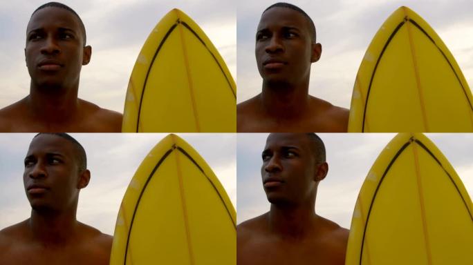 非裔美国男性冲浪者站在海滩4k冲浪板前视图