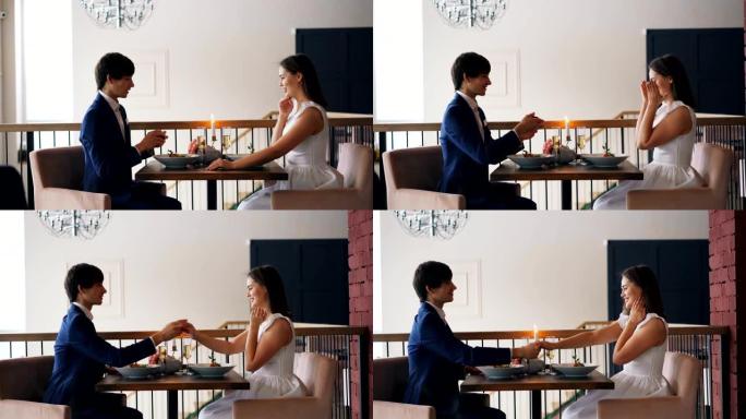 充满爱心的年轻人正在餐厅里向快乐的女孩求婚，坐在餐桌旁，给她一枚戒指，然后亲吻她的手。开始家庭和约会