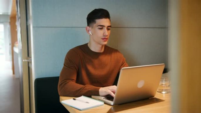 年轻人独自在办公室食堂摊位的桌子上的笔记本电脑上工作，有选择地集中精力