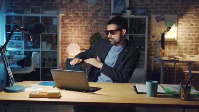 戴着眼镜的快乐男人在黑暗的办公室里享受着与笔记本电脑一起跳舞的音乐