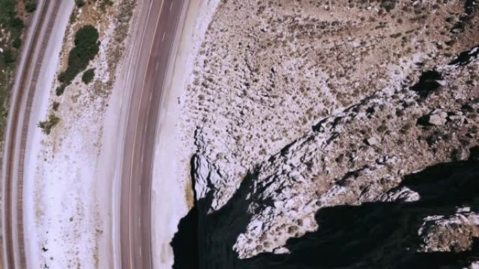 俯视图无人机在美丽的高速公路和铁轨上右转，靠近史诗般的岩石砂岩山。