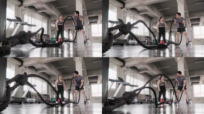 (慢动作) 超重的妇女和教练在健身馆进行战斗绳索运动。