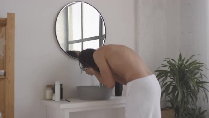 帅哥在水槽边洗脸，在浴室镜子里看