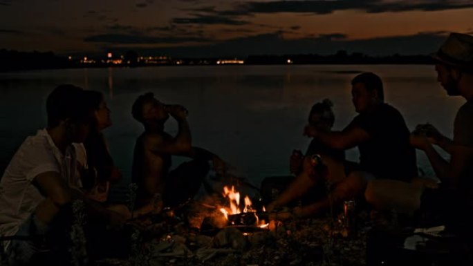 SLO MO年轻人在湖边的篝火旁喝酒