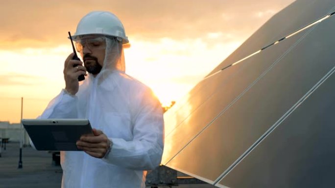 屋顶上的日落景观，男性专家在太阳能电池旁边的发射器上讲话