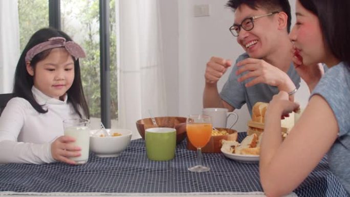亚洲日本家庭在家里吃早餐。早上在厨房的桌子上吃面包，玉米片谷物和牛奶时，亚洲妈妈，爸爸和女儿在一起聊